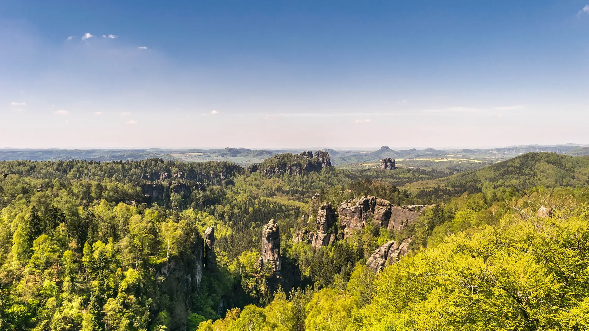 Weitläufige Landschaft mit bewaldeten Hügeln und markanten Felsformationen unter blauem Himmel