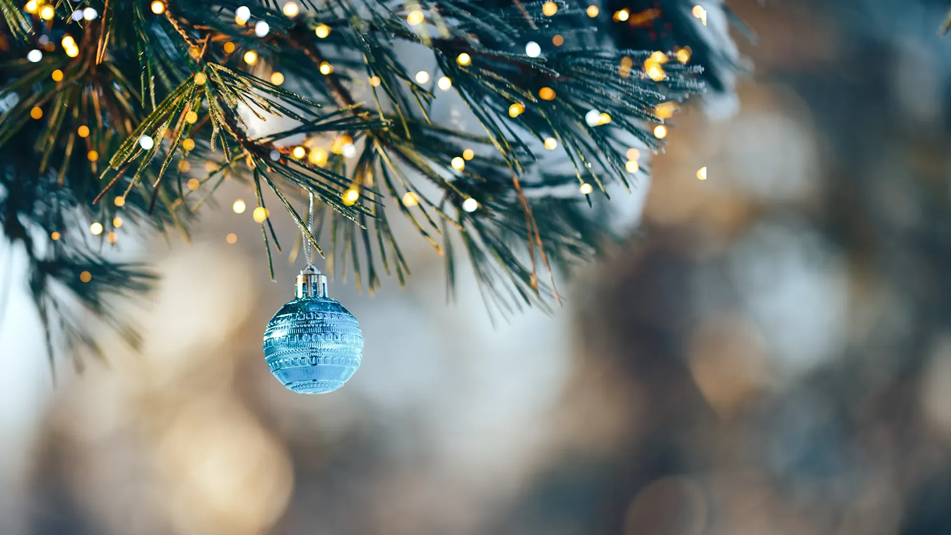 Nahaufnahme eines blauen Christbaumkugelschmucks an einem Tannenzweig mit unscharfem Hintergrund und Lichterkettenbeleuchtung