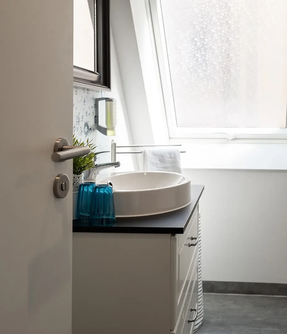 Badezimmer mit rundem Waschbecken auf schwarzer Arbeitsplatte, Handtuchhalter und mattiertem Fenster