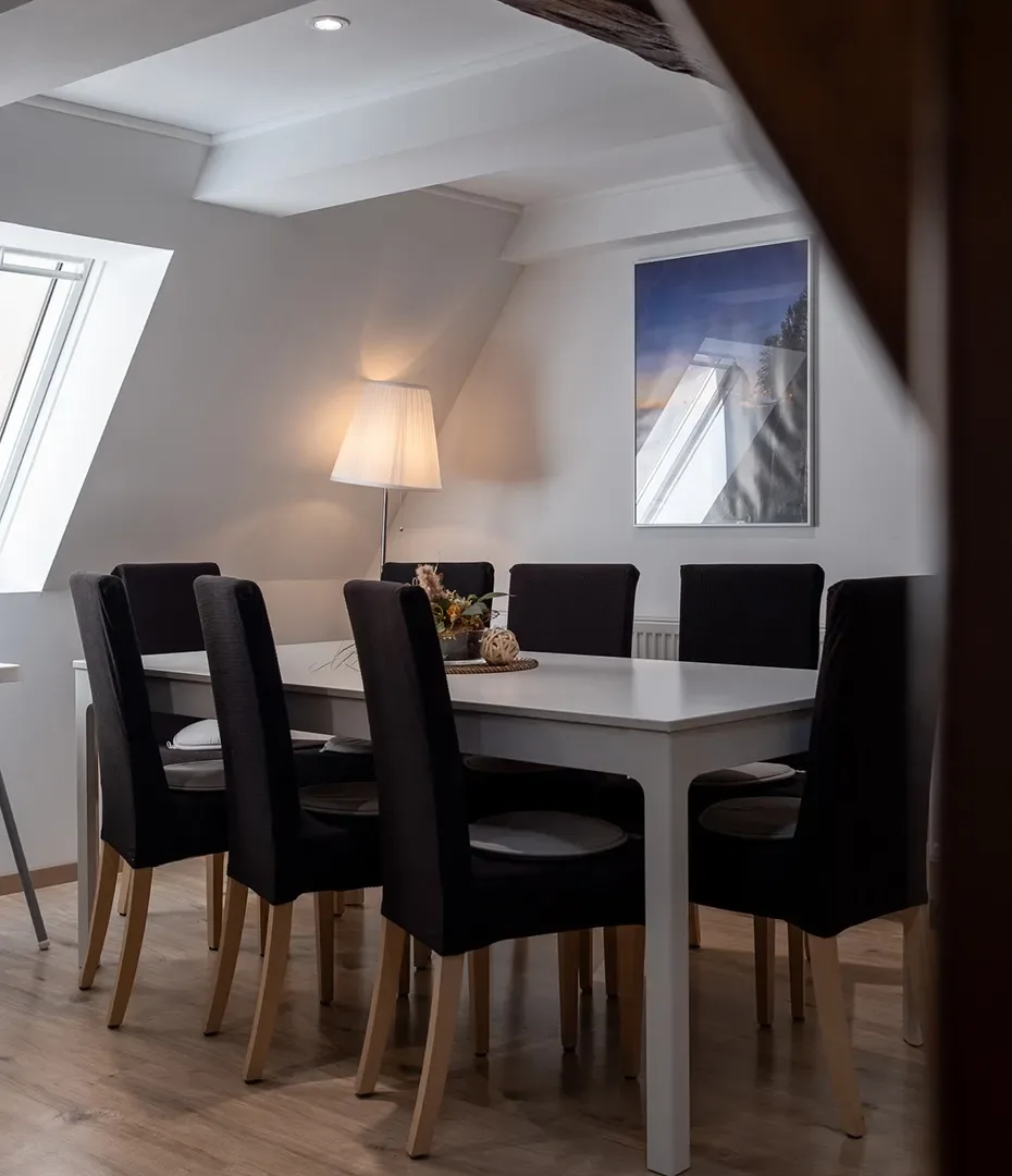 Essbereich mit weißem Tisch, sechs schwarzen Stühlen mit Holzbeinen, Stehlampe und Dachschräge
