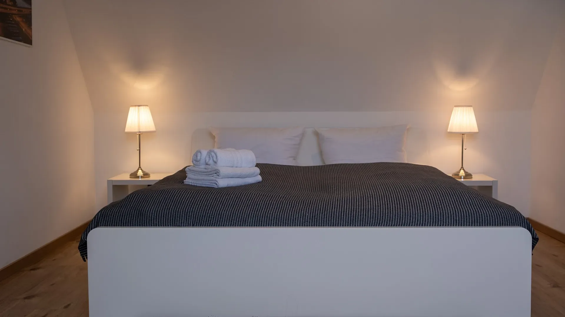 Schlafzimmer mit großem Doppelbett, zwei Nachttischen mit Lampen und gefalteten Handtüchern auf der Bettdecke