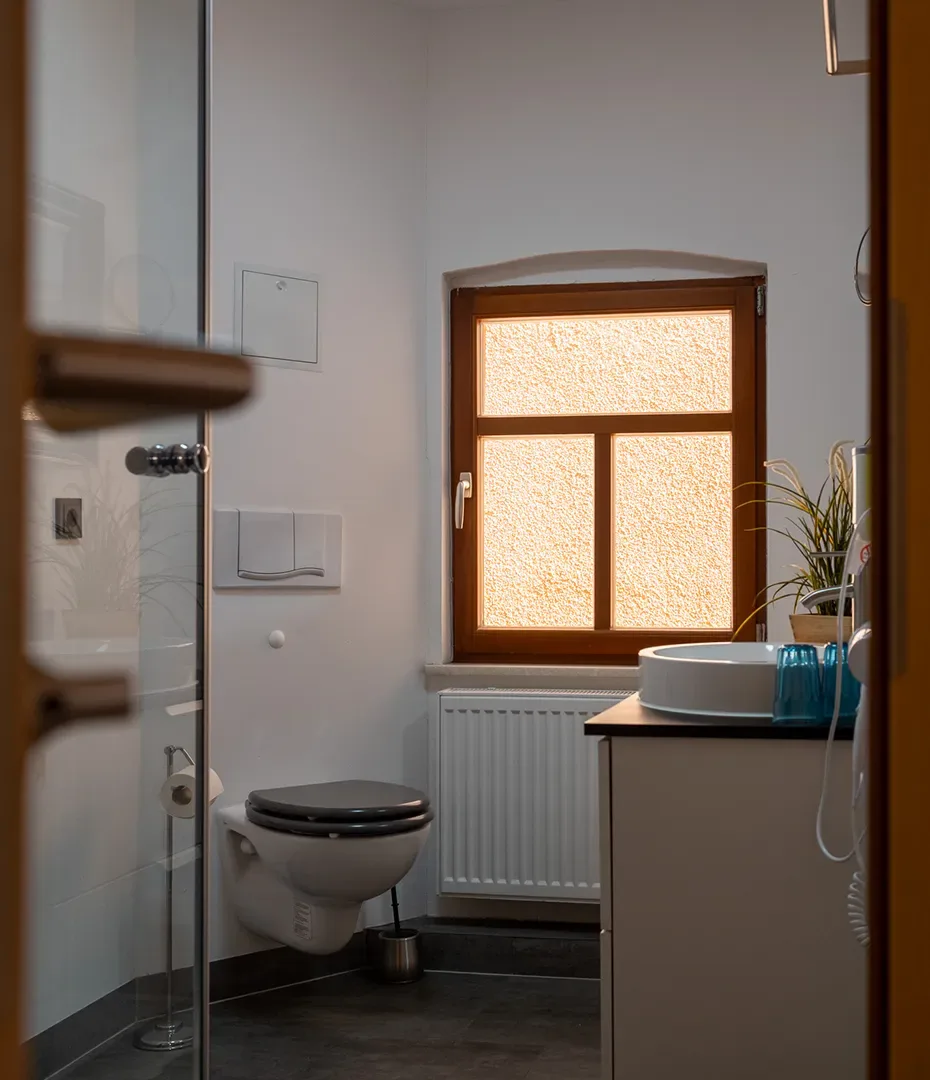 Badezimmer mit Wand-WC, Waschbecken auf Holzplatte, Fenster und Pflanzen