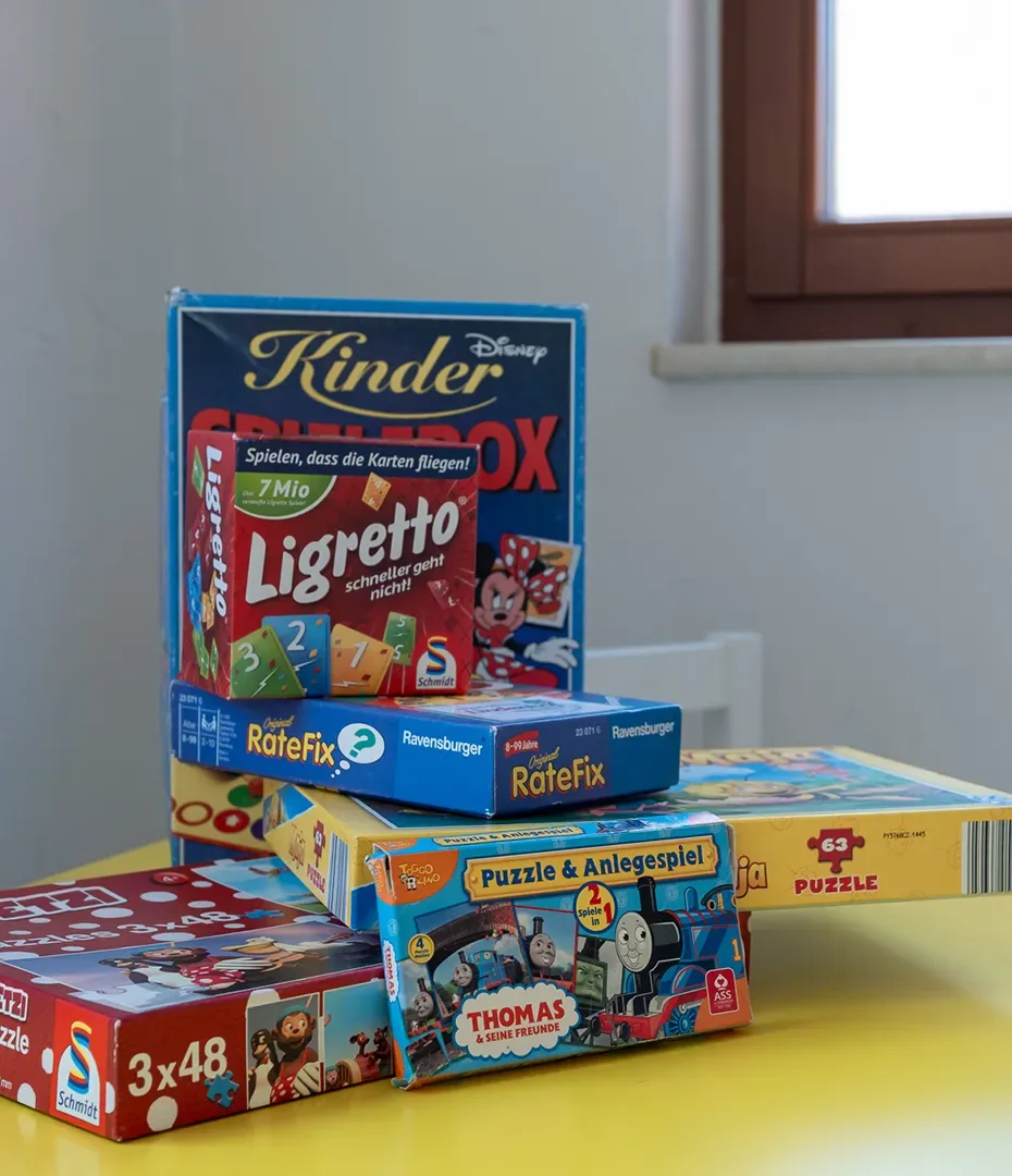 Mehrere Gesellschafts- und Puzzlespiele wie Ligretto, RateFix und Thomas & seine Freunde auf einem gelben Tisch vor einem Fenster