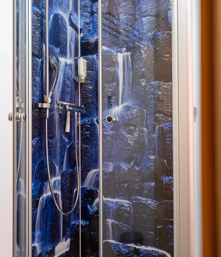 Dusche mit Duschwand, die mit einem Fotomotiv von Wasserfällen und Felsen bedruckt ist