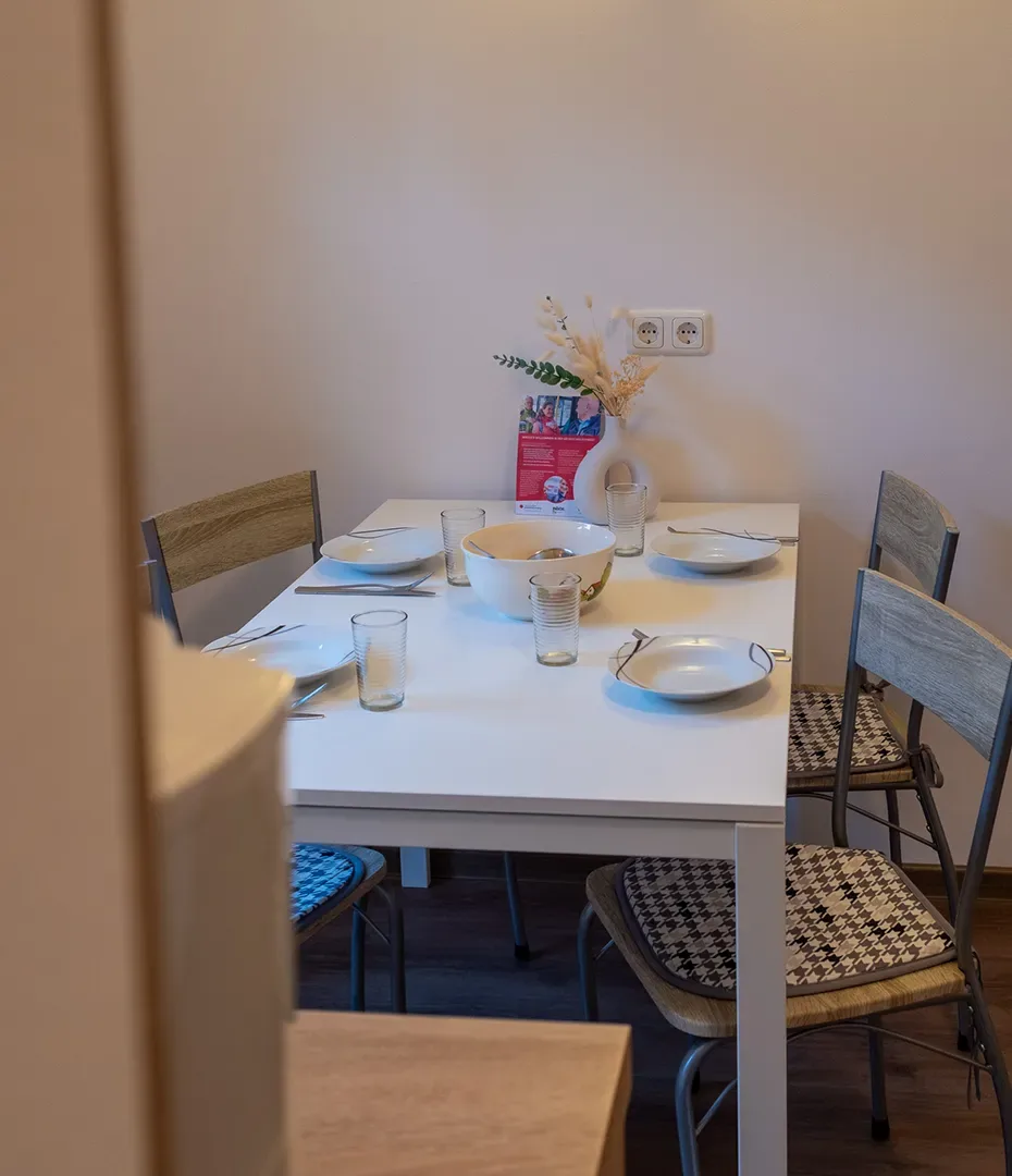 Essbereich mit weißem Tisch, vier Stühlen mit gemusterten Sitzkissen, Tellern, Gläsern und einer Blumendekoration auf dem Tisch