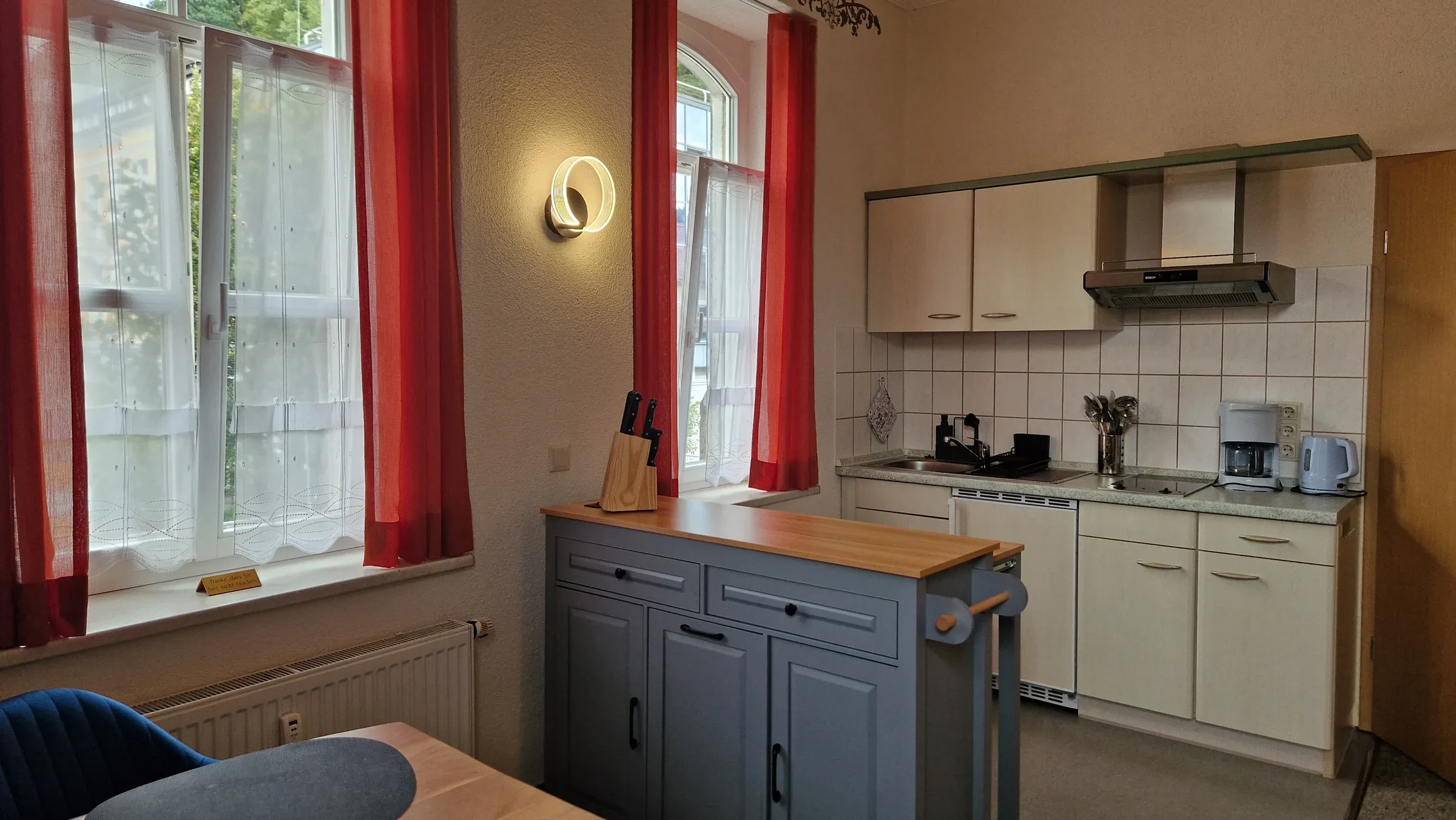 Küchenzeile mit weißen Oberschränken, Dunstabzugshaube, Kaffeemaschine und grauer Kücheninsel mit Holzarbeitsplatte