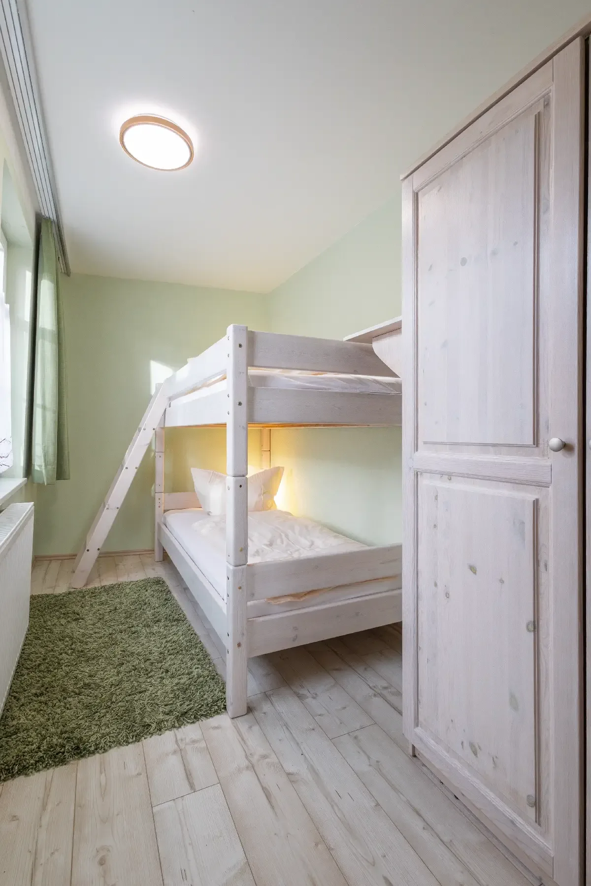 Kleines Schlafzimmer mit weißem Etagenbett, grünem Teppich und kleinem weißen Schrank