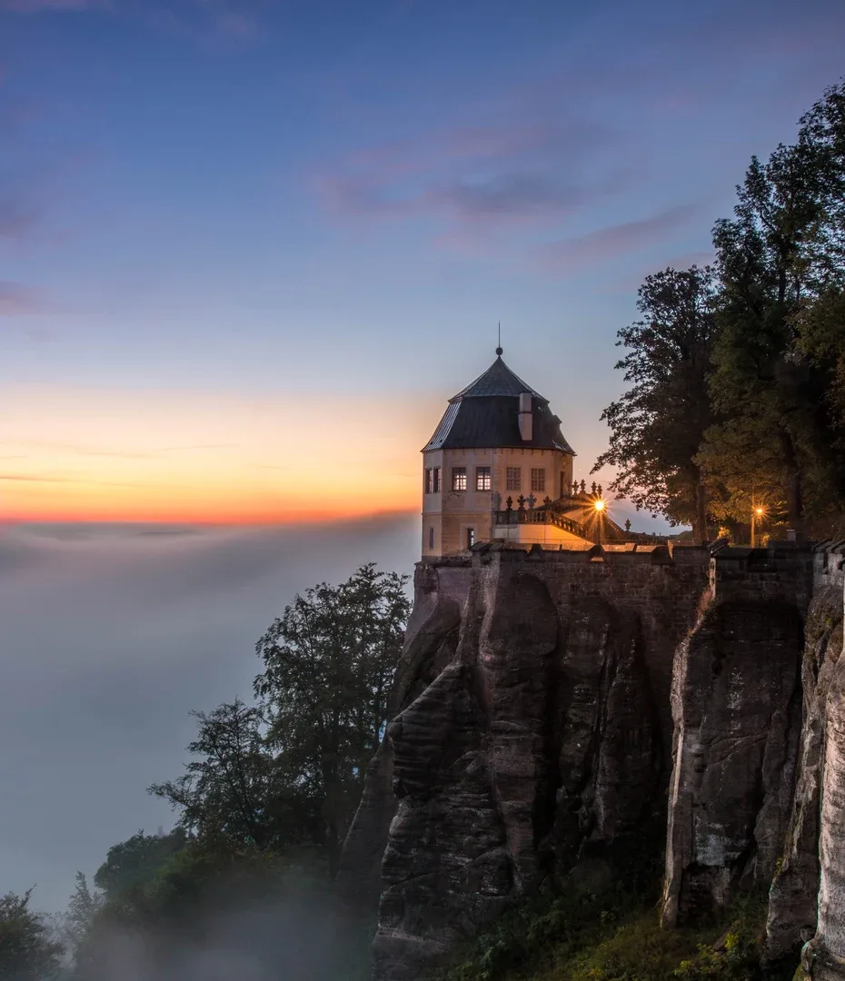 Festung Königstein auf einem Felsplateau bei Sonnenaufgang über einem Nebelmeer