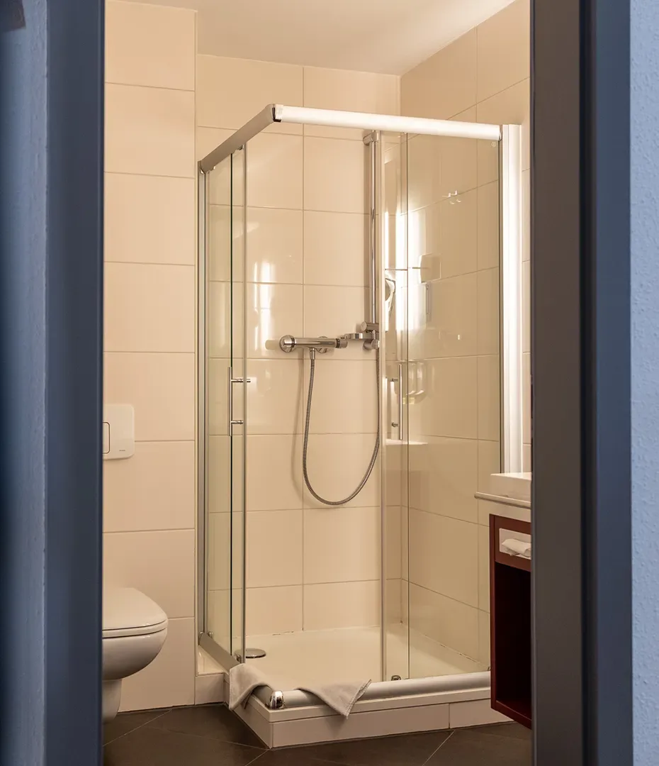 Kleine Hotelbadezimmer mit Duschkabine aus Glas, Toilette und Waschtisch mit Handtuchfach