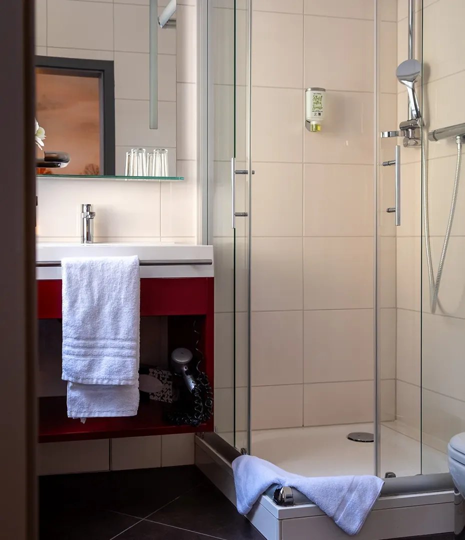 Badezimmer mit Glasdusche, Handtüchern, Waschbecken und Spiegel