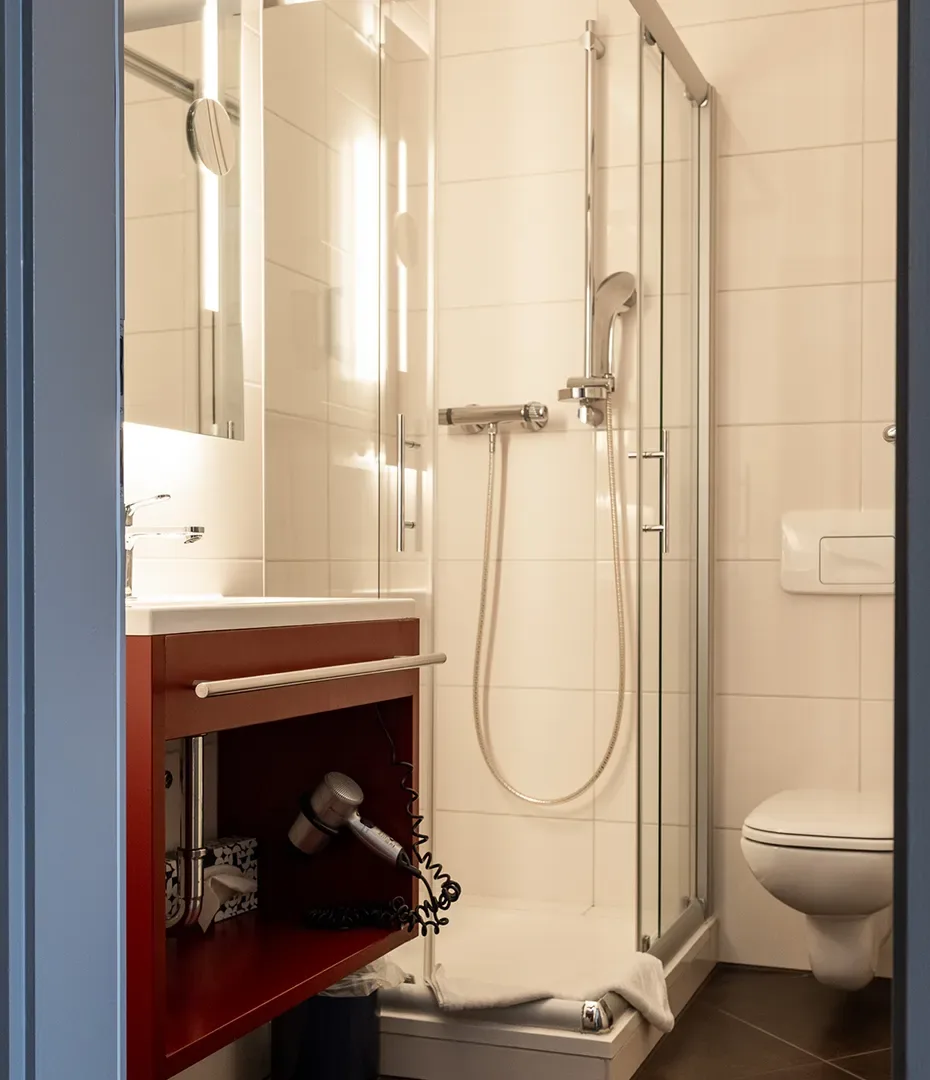 Kleines Badezimmer mit Duschkabine, Toilette, Waschbecken und Föhn in offenem Regal