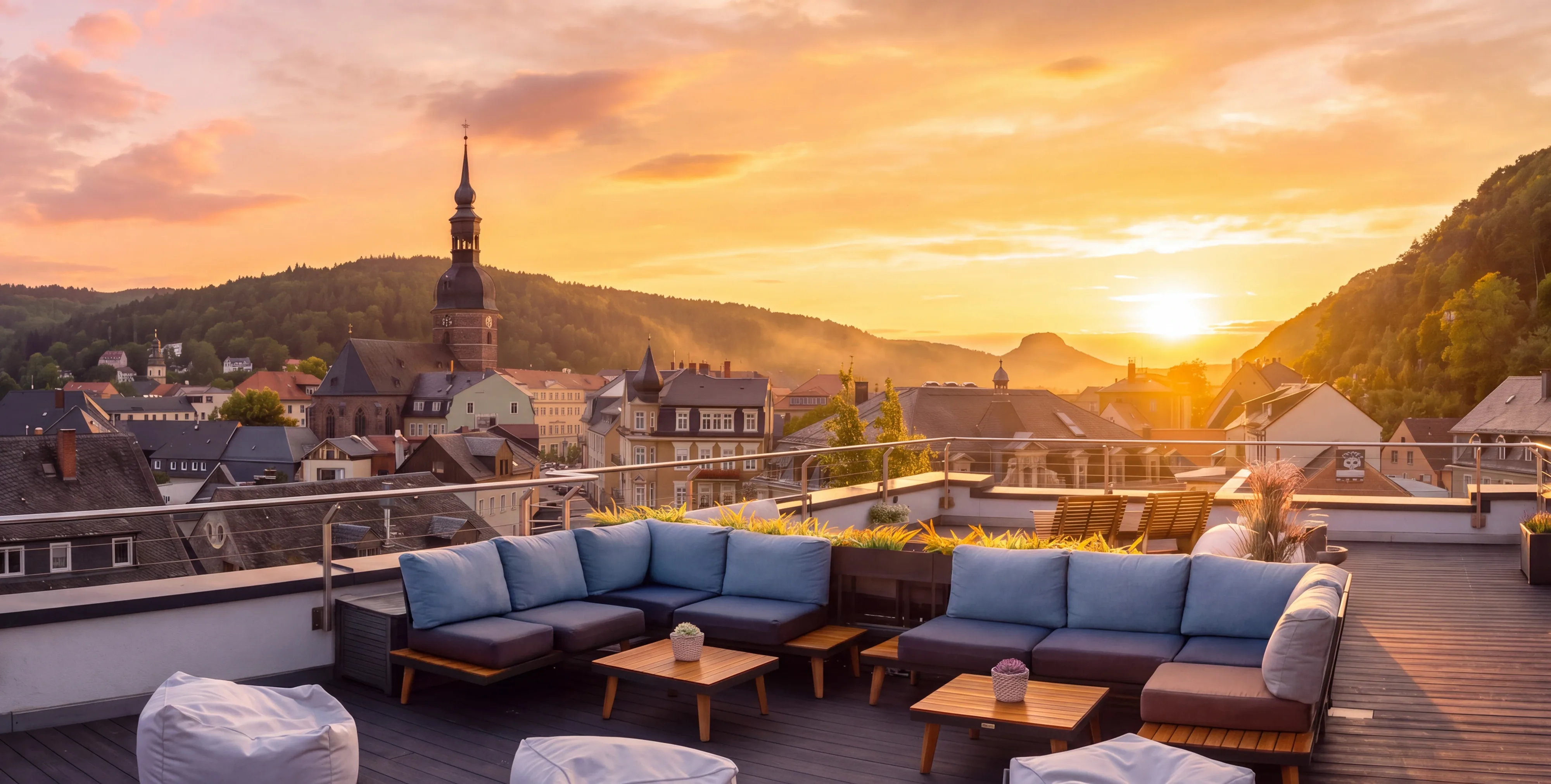 Blick von einer Dachterrasse über die Dächer von Bad Schandau bei Sonnenuntergang mit bewaldeten Hügeln im Hintergrund