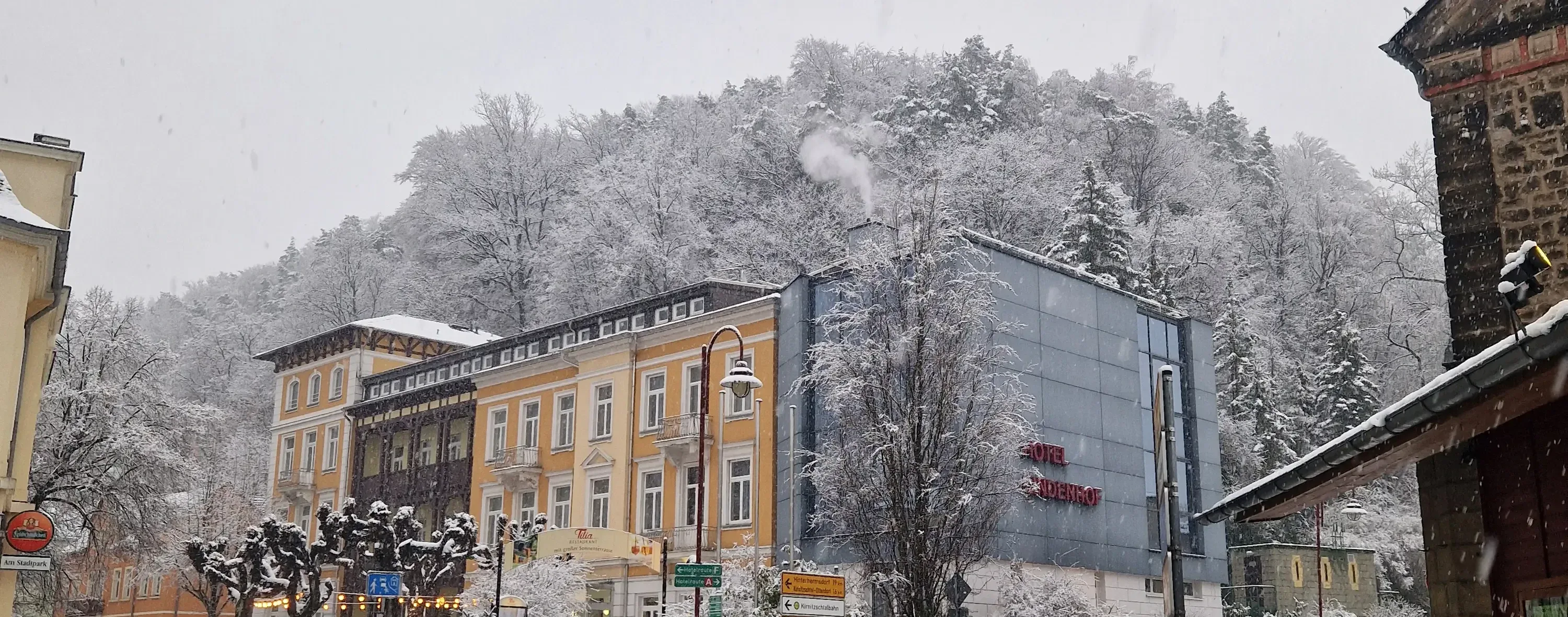 Hotelgebäude mit gelber Fassade und modernem Anbau vor schneebedecktem Wald im Winter