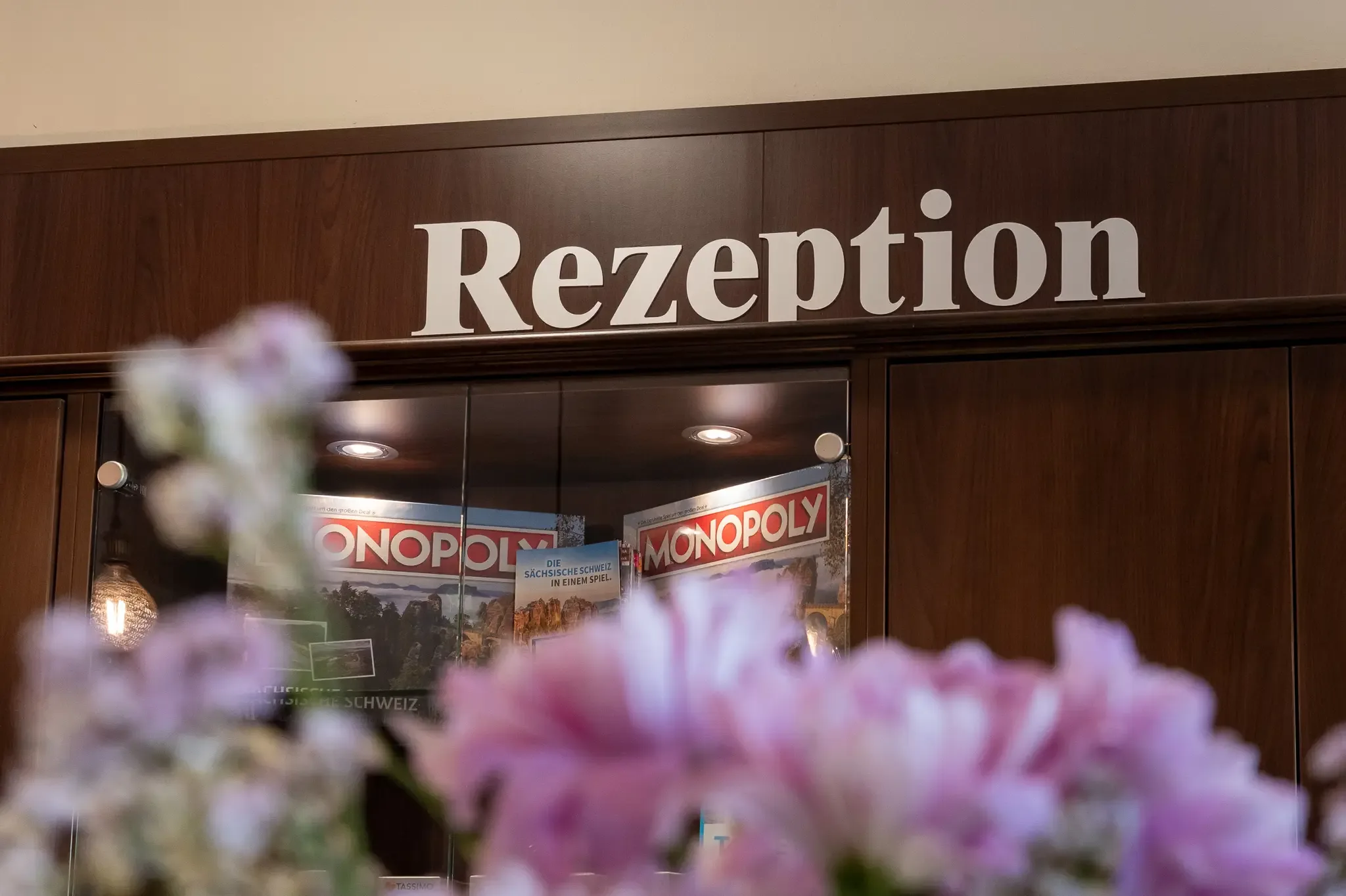 Holzvertäfelte Hotelrezeption mit dem Schriftzug 'Rezeption' und Monopoly-Spielen im Regal dahinter