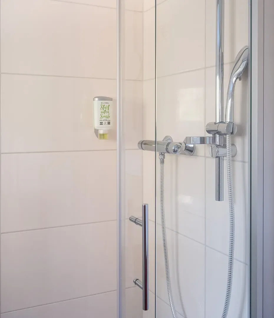 Dusche mit Glasabtrennung, verchromtem Duschkopf und Duscharmatur an weiß gefliester Wand