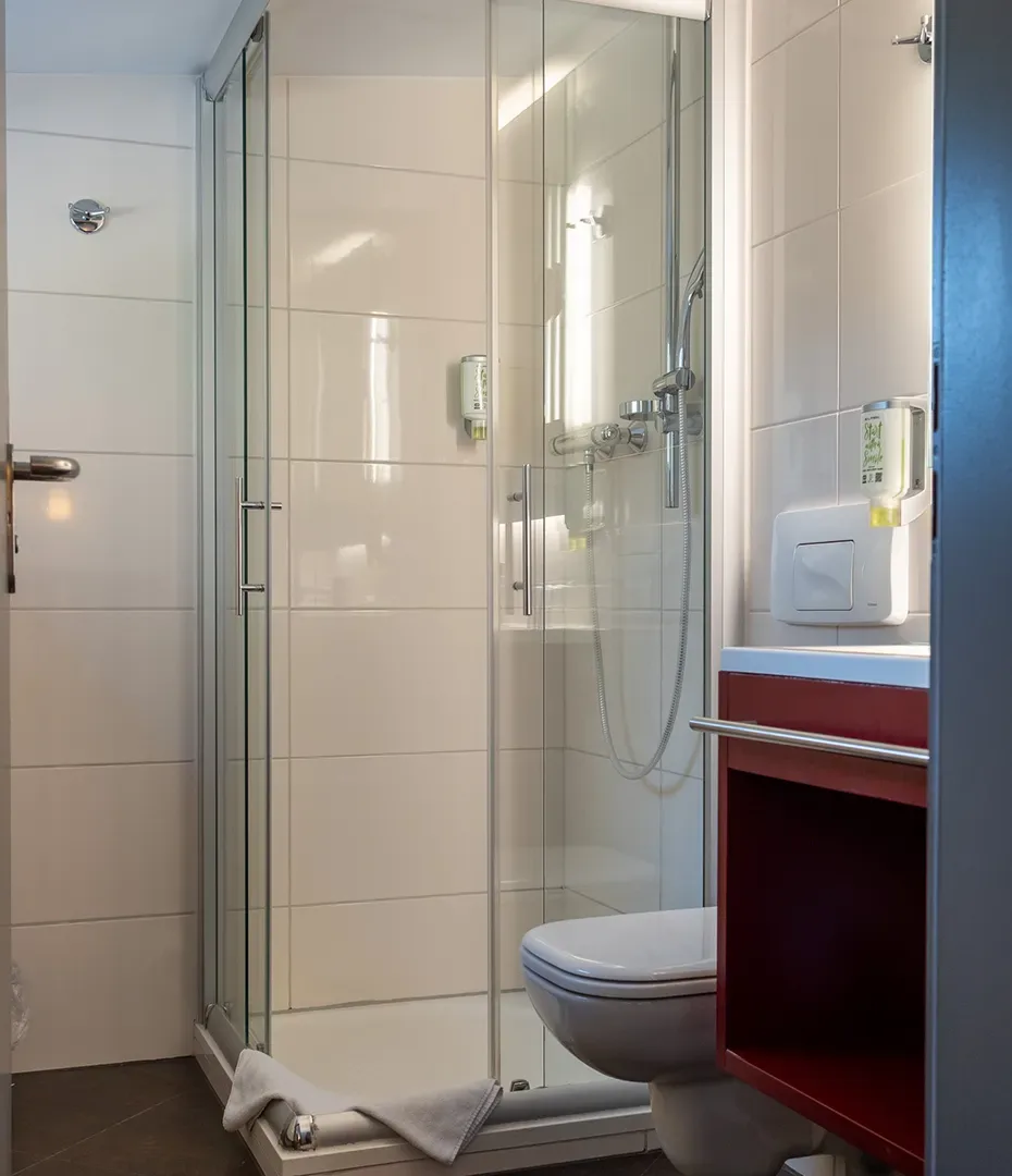 Kleines Badezimmer mit Glasdusche, wandhängendem WC und rotem Unterschrank unter dem Waschbecken