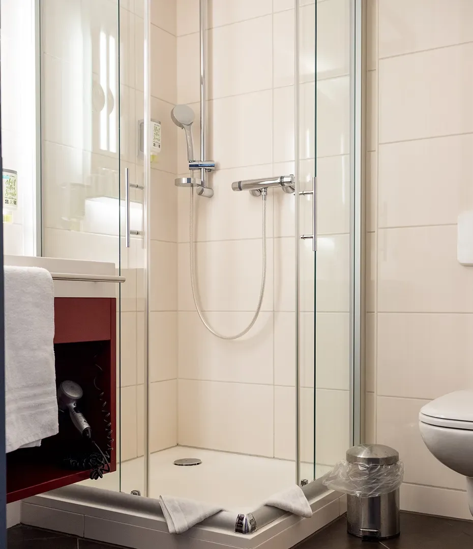 Kleine Badezimmerdusche mit Glasabtrennung, Handbrause, Handtuch und Mülleimer