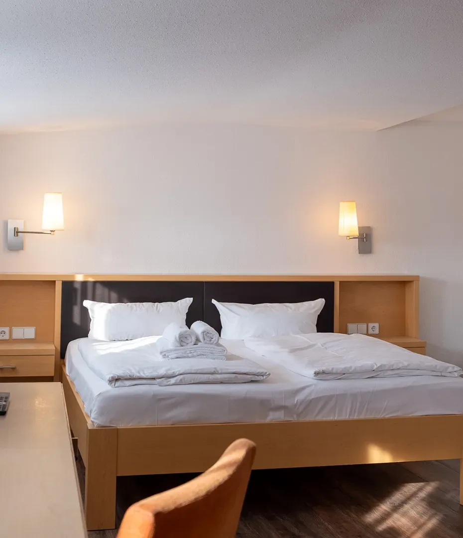 Doppelbett mit weißen Kissen und Bettwäsche in einem hellen Zimmer mit zwei Wandlampen und einem Holzkopfteil