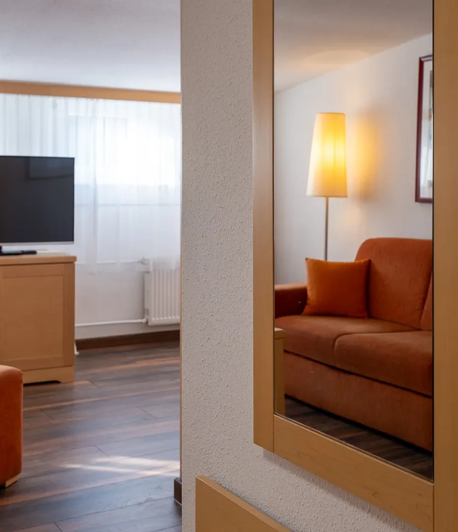 Spiegel an einer Wand, der eine orangefarbene Couch mit Kissen und eine Stehlampe in einem Zimmer reflektiert
