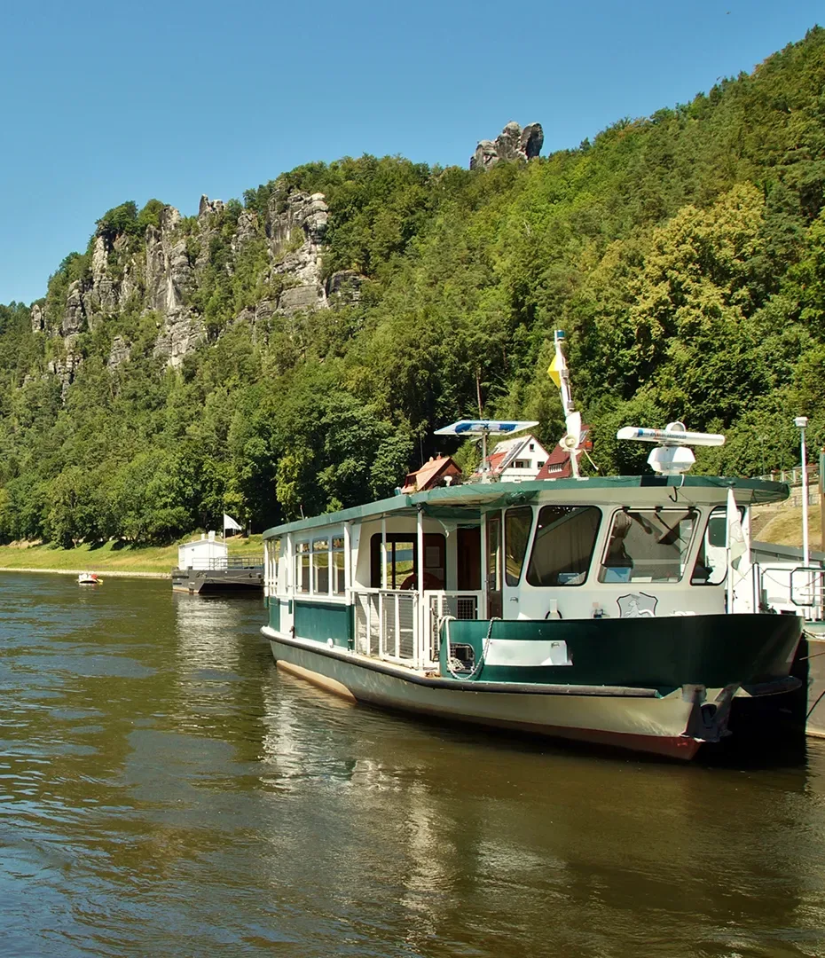 Fahrgastschiff auf einem Fluss vor bewaldeten Felsen