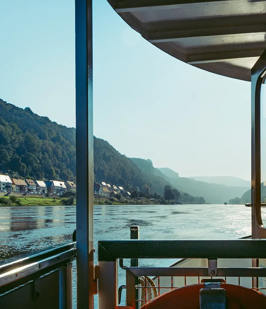 Blick von einem Schiff auf einen Fluss mit bewaldeten Hügeln und Häusern am Ufer