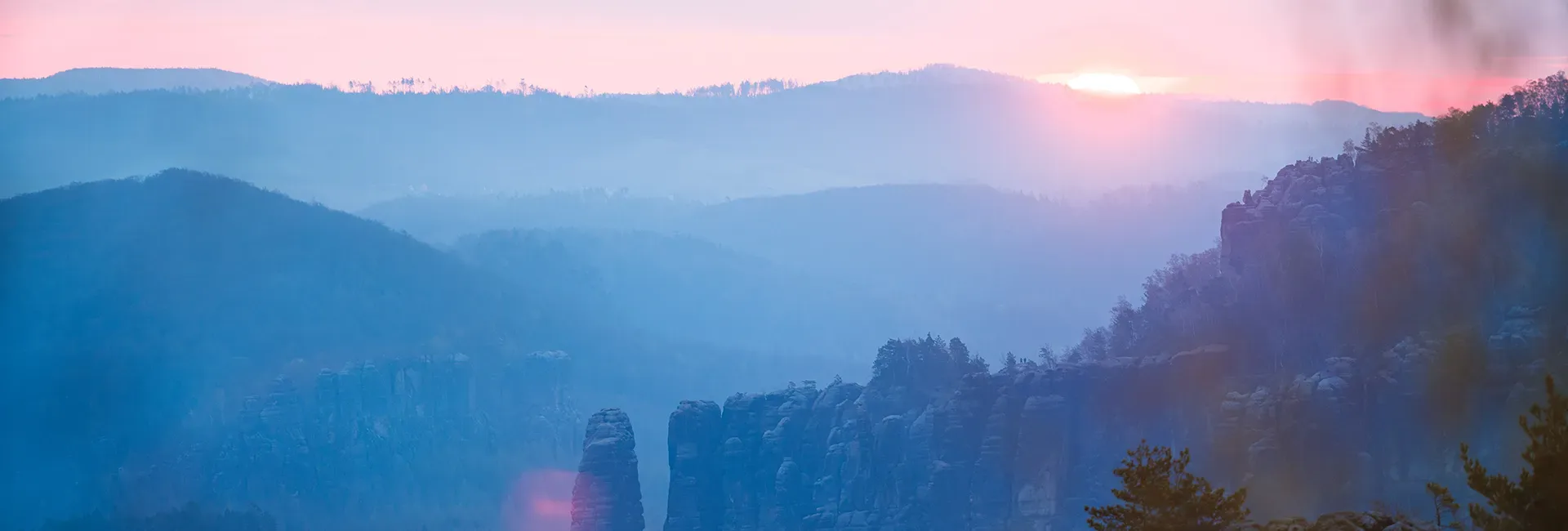 Berglandschaft mit Felsen und Wald im Dunst bei Sonnenaufgang oder Sonnenuntergang