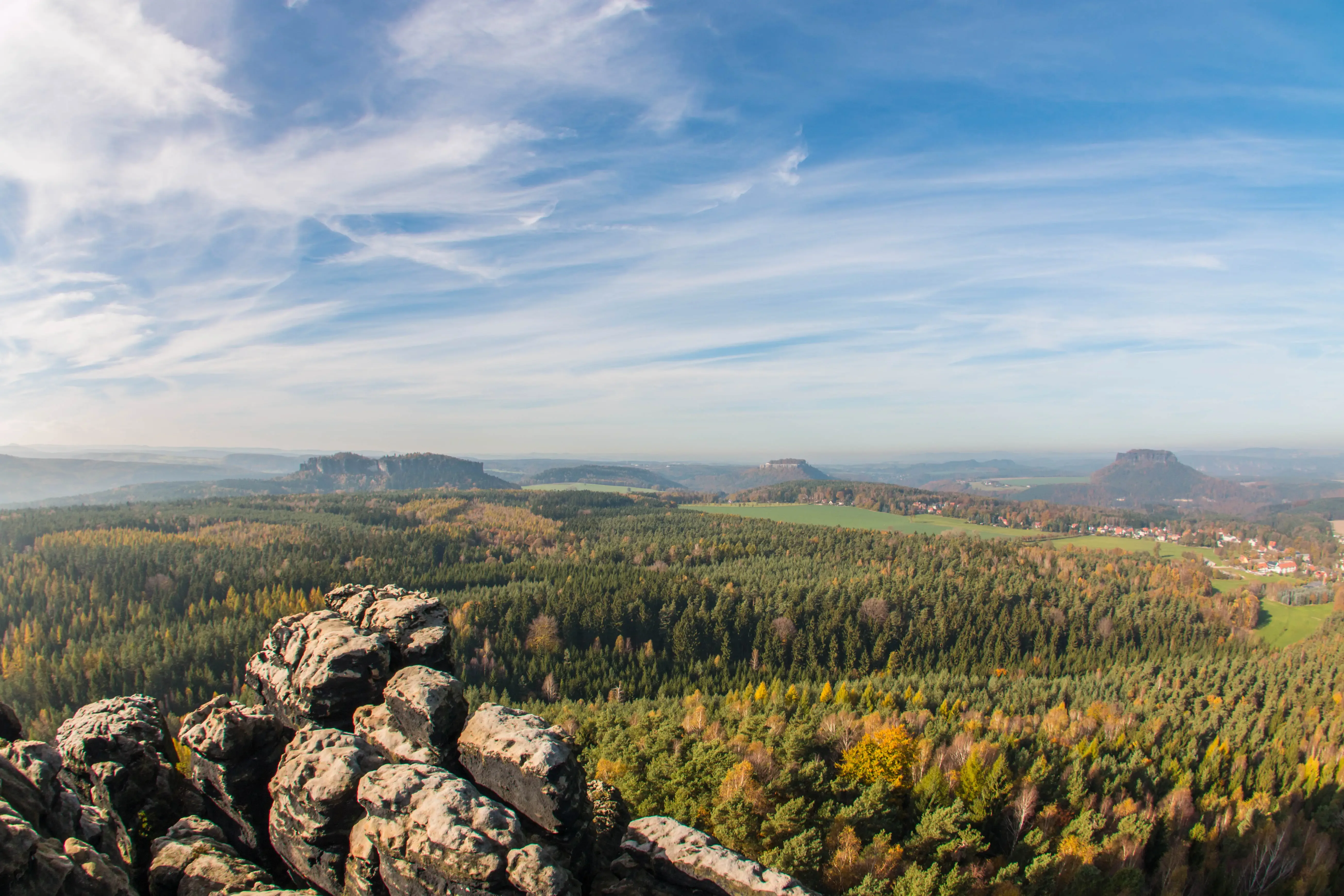 Felsformation im Vordergrund mit weiter Waldlandschaft und markanten Tafelbergen am Horizont unter blauem Himmel mit Wolken