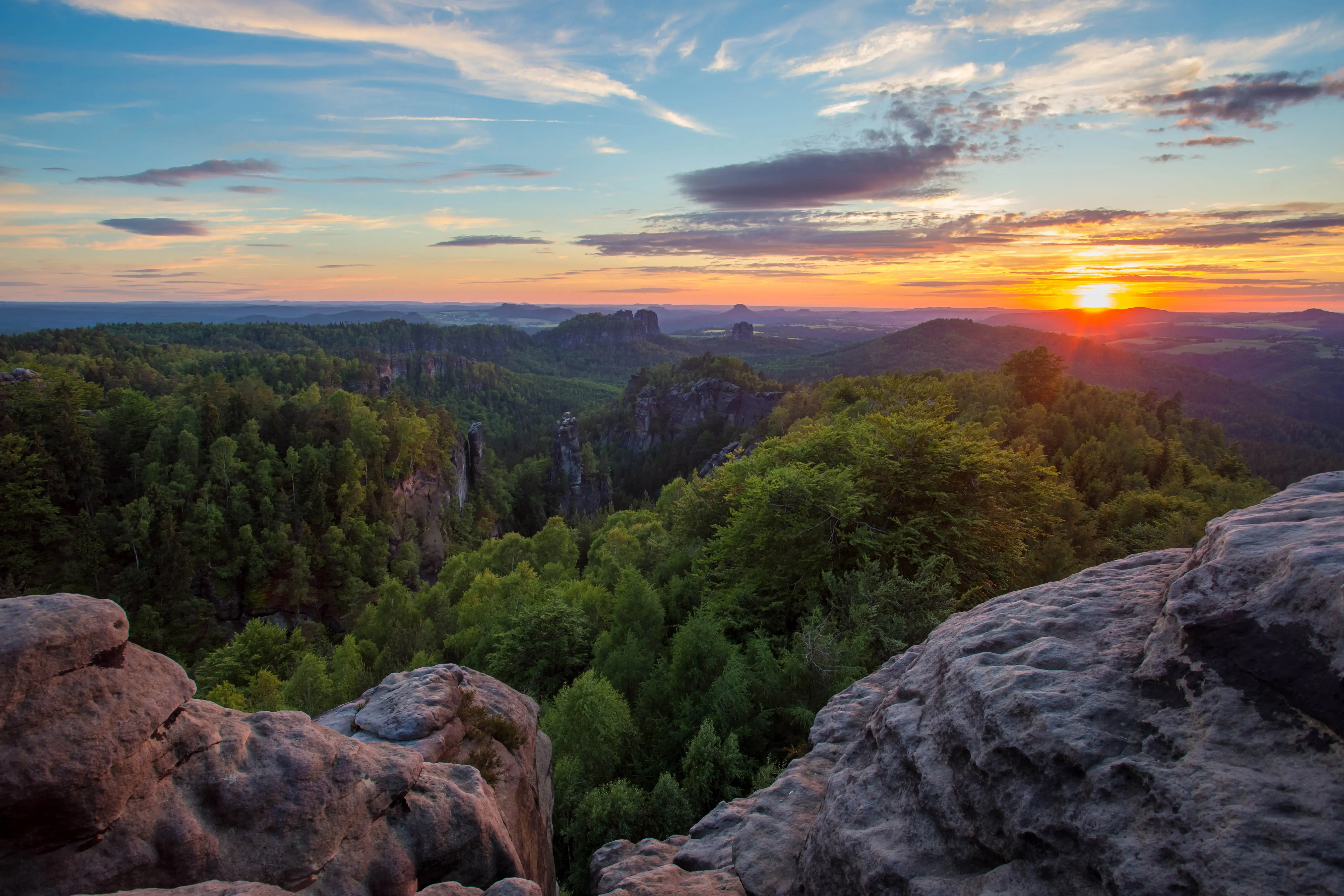 Felsvorsprung mit Blick auf bewaldete Felsenlandschaft und Sonnenuntergang am Horizont
