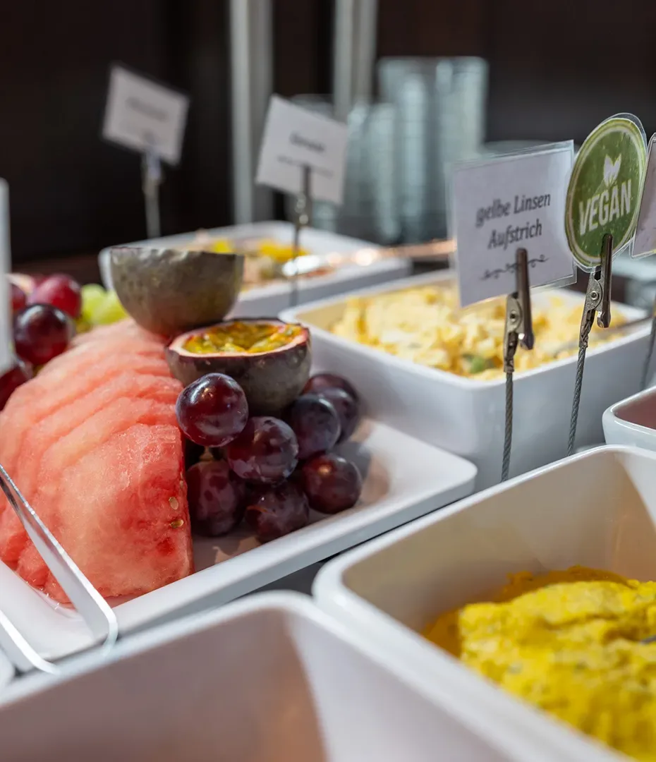 Frühstücksbuffet mit Wassermelone, Trauben, Passionsfrucht und veganem gelben Linsenaufstrich in weißen Schalen