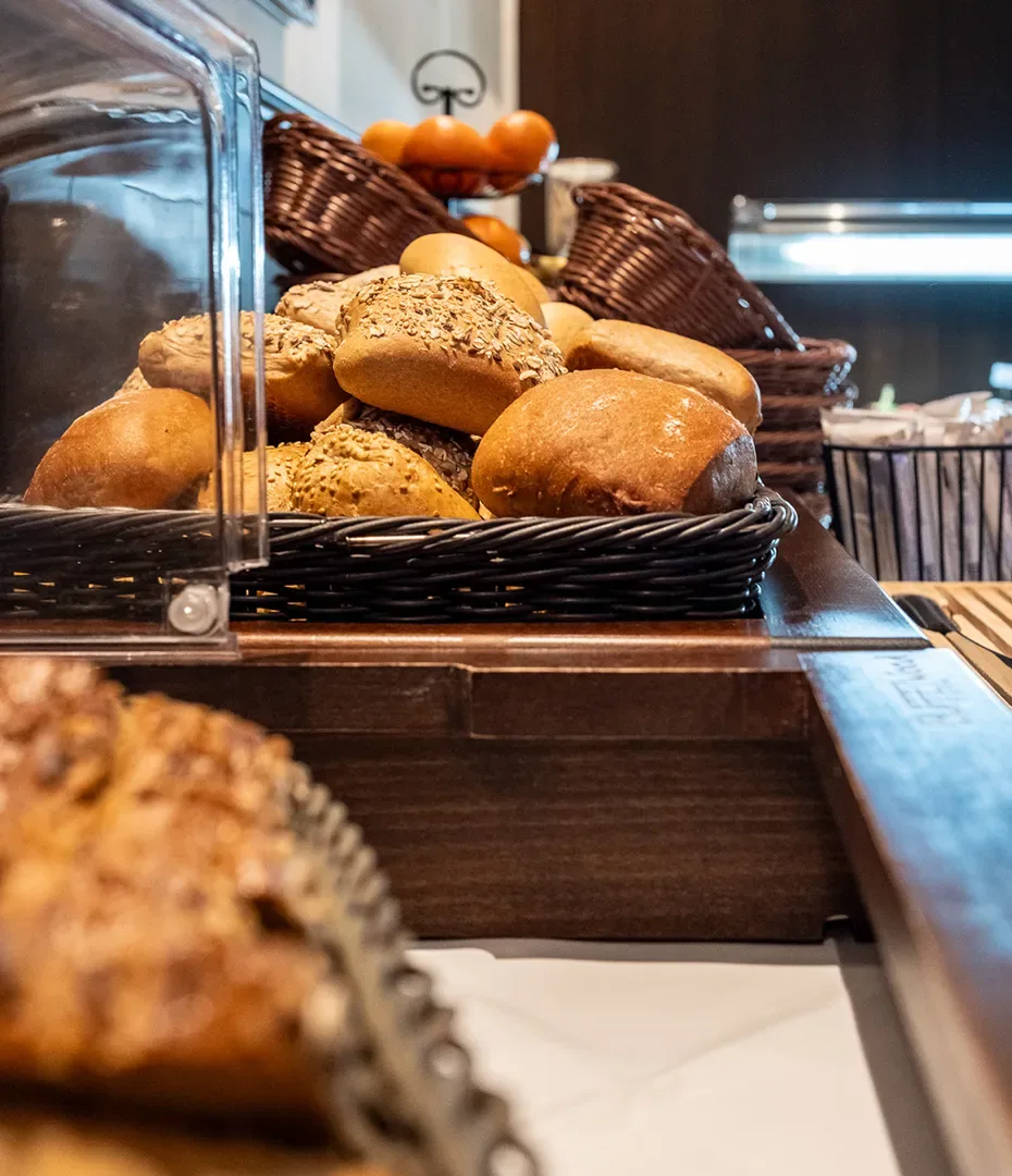 Verschiedene Brötchen in einem Korb auf einem Holztisch mit weiteren Körben und Orangen im Hintergrund
